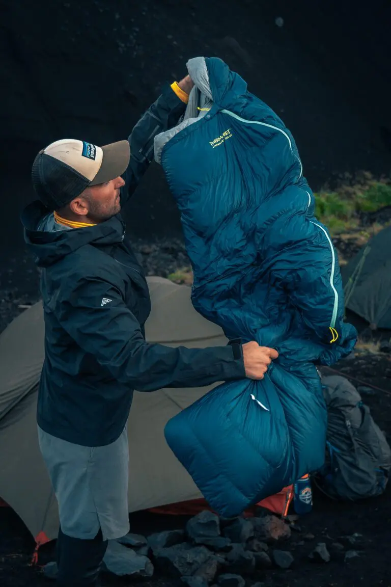 homme rangeant un sac de couchage bleu devant une tente