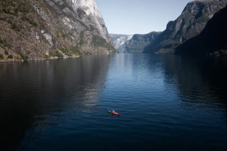 kayakiste pagayant dans un kayak rouge sur un fjord bleu profond