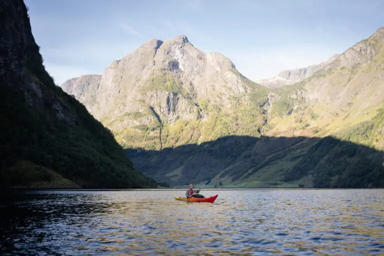 personne faisant du kayak sur un fjord entouré de montagnes