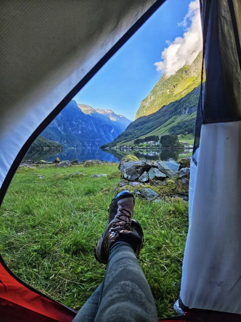 jambes et bottes d’une personne dans une tente donnant sur un fjord
