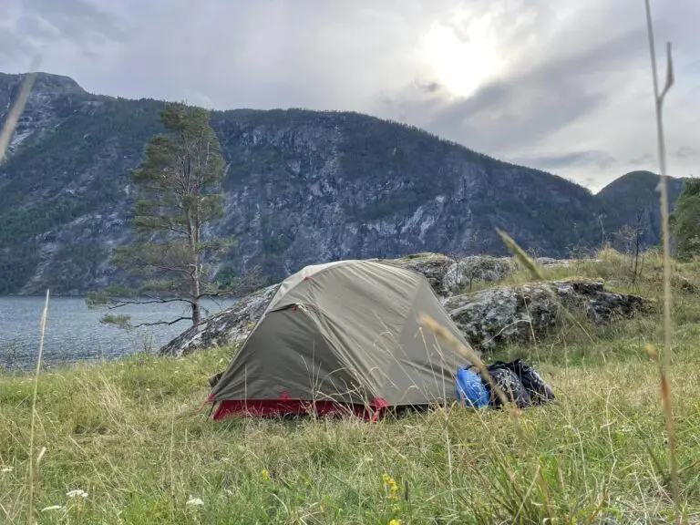 tente installée au bord d’un lac, avec des montagnes sous un ciel nuageux