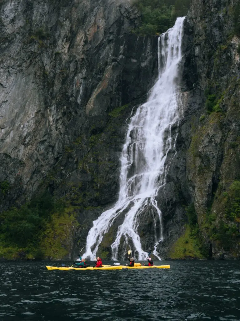 des kayakistes pagayant devant une grande cascade dans un fjord