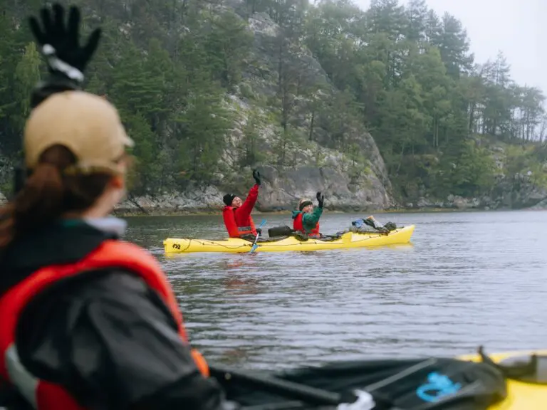 three people kayaking on a lake with forested cliffs