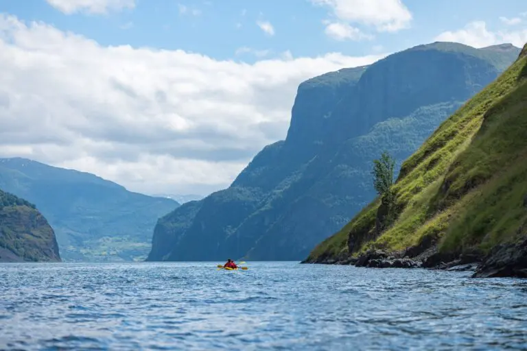 kayakiste pagayant dans un fjord norvégien bordé de montagnes escarpées