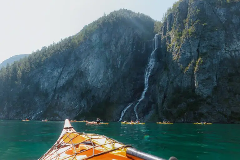 des kayakistes pagayant devant une grande cascade dans un fjord