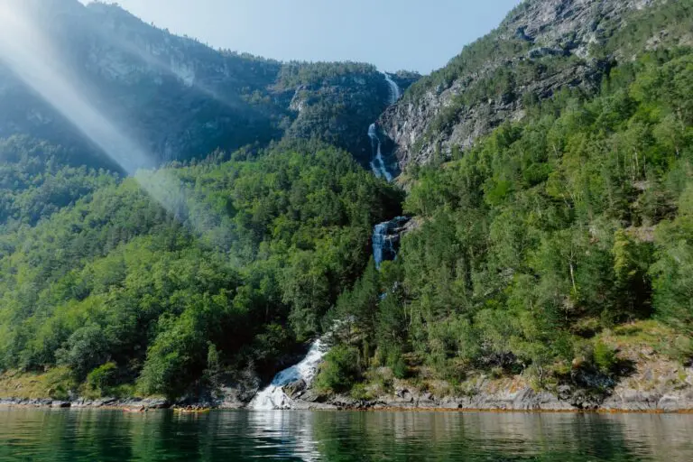 kayakistes sur un fjord avec une cascade et des rayons de soleil