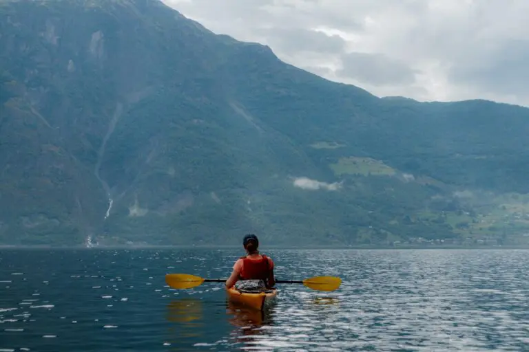 personne faisant du kayak sur un lac calme, avec des montagnes en arrière-plan