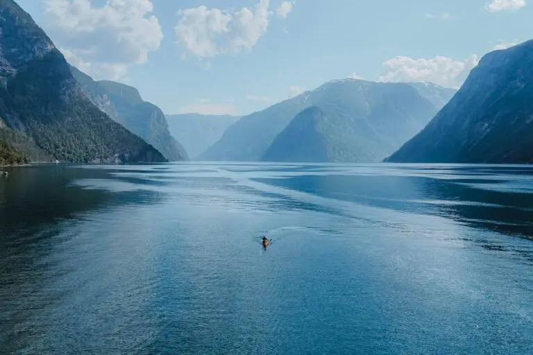 kayaker paddling in a vast fjord surrounded by mountains