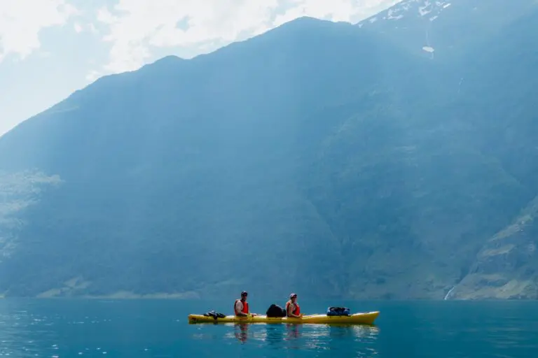 deux personnes faisant du kayak sur un lac calme entouré de montagnes