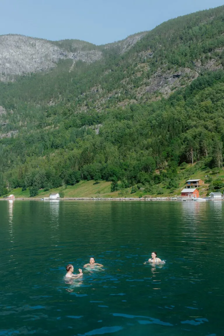 trois femmes nageant dans un fjord verdoyant entouré de montagnes