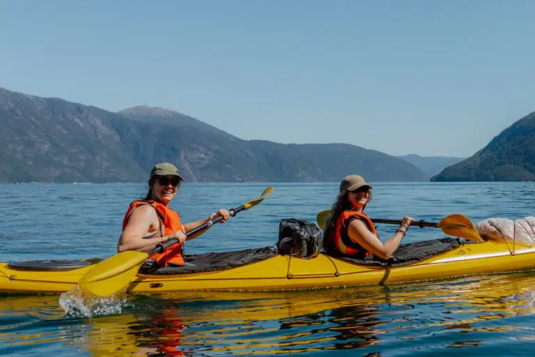deux femmes faisant du kayak sur un lac, avec des montagnes en arrière-plan