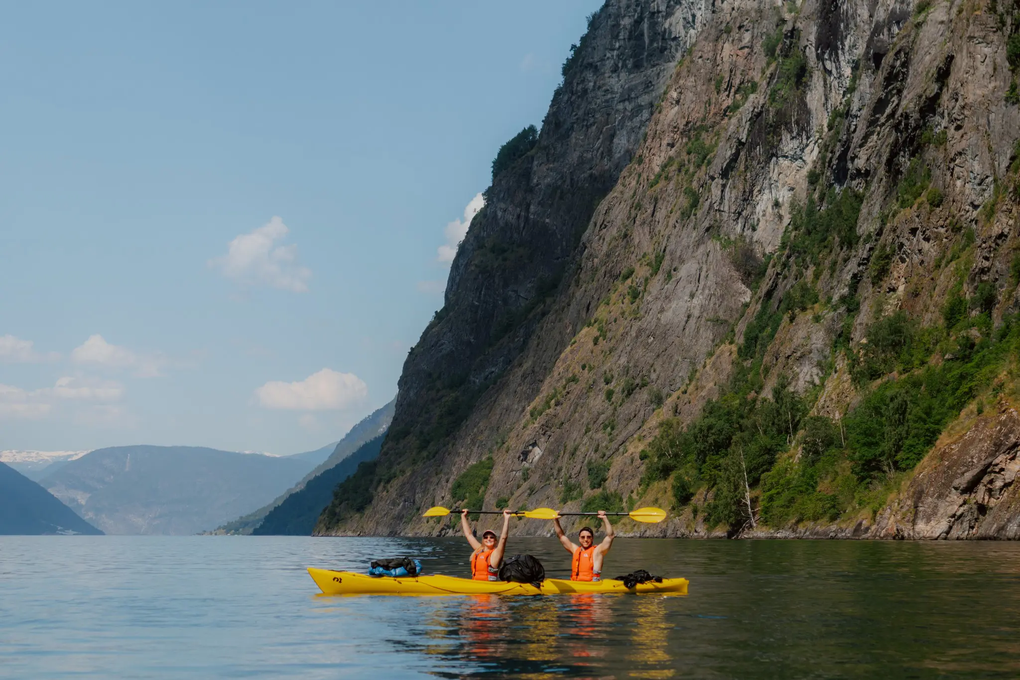 two people kayaking in a fjord, paddles raised in celebration